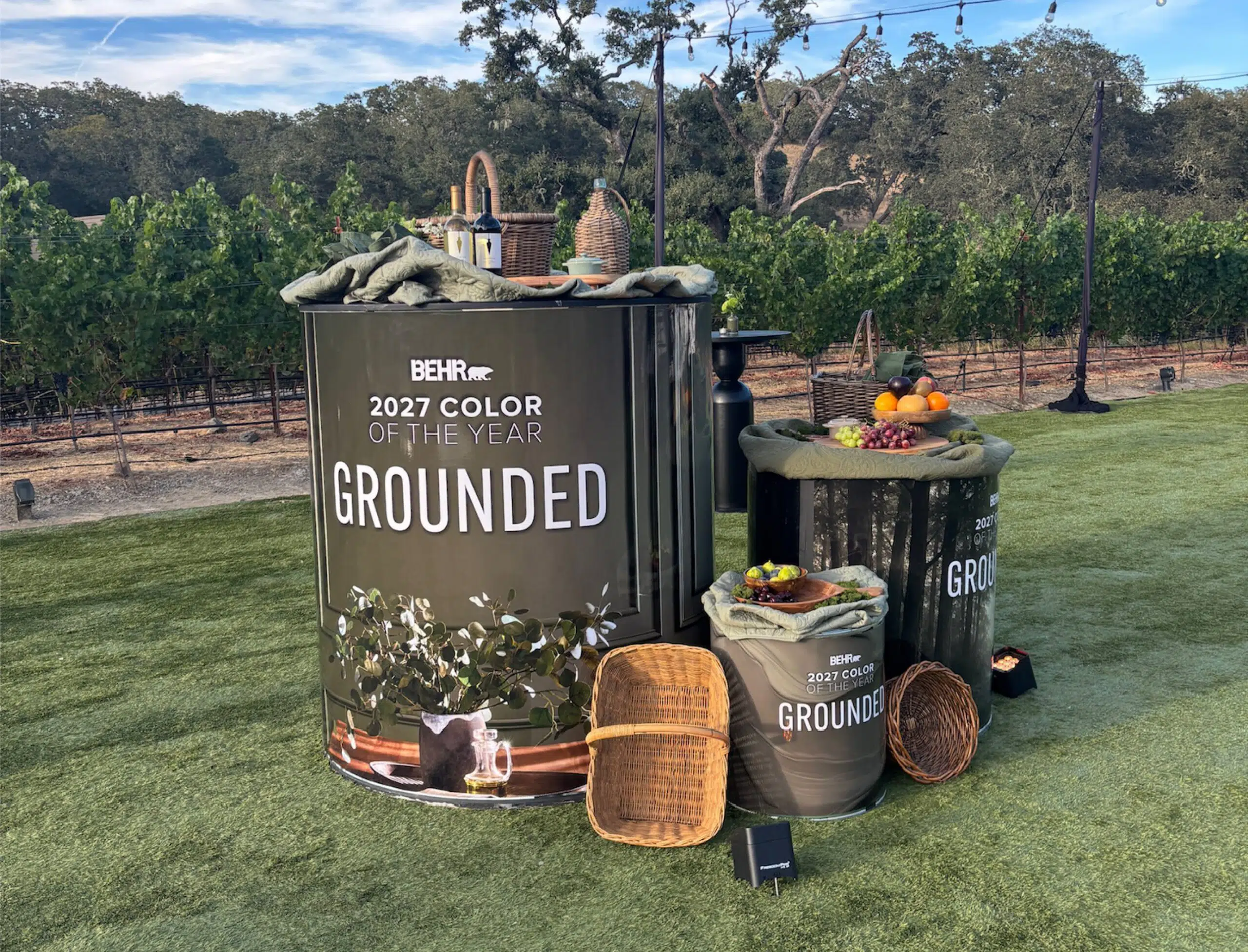 Behr 2027 Color of the Year Grounded paint can display with picnic props in a vineyard